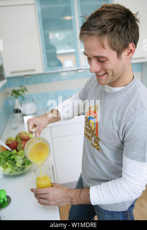 Junger Mann, gießen ein Glas Orangensaft, München, Deutschland Stockfoto