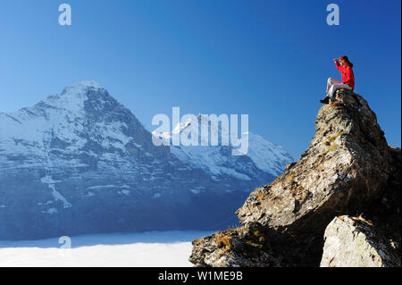 Frau auf den Felsen sitzen und den Blick auf Eiger und Jungfrau über dem Meer von Nebel, Bussalp, Grindelwald, UNESCO Welterbe Schweizer Alpen Jungfrau - Stockfoto