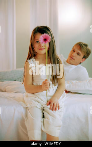 Mädchen mit Gerbera auf Bett mit Vater, Porträt Stockfoto