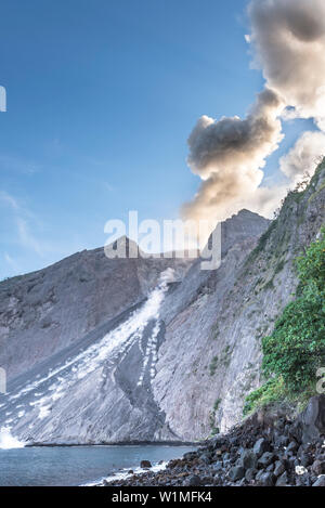 Grosse Ascheeruption mit auswürfen von Felsen am brennenden Rand von Batu Tara in der Flores See mit Leuchtdioden vulkanische Gase und Asche mit blauem Himmel. Ston Stockfoto