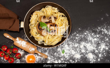 Tagliatelle mit frischen Champignons und Basilikum in einer Pfanne auf schwarzen Hintergrund mit kopieren. Ansicht von oben. Stockfoto