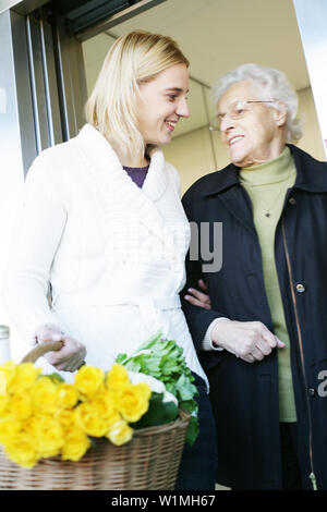 Junge Frau hilft, eine ältere Dame und trägt das Einkaufen Stockfoto