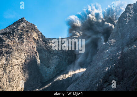 Grosse Ascheeruption mit auswürfen von Felsen am brennenden Rand von Batu Tara in der Flores See mit Leuchtdioden vulkanische Gase und Asche und blauer Himmel. Stony Stockfoto