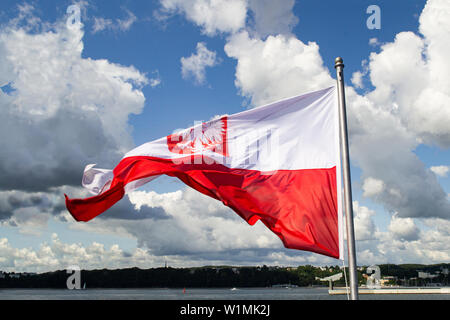 Flagge Polens. Polen Nationalflagge mit Wappen an bewölkten Himmel. Ostseeküste, Blick vom Schiff. Windiges Wetter Stockfoto