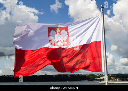 Flagge Polens. Polen Nationalflagge mit Wappen an bewölkten Himmel. Ostseeküste, Blick vom Schiff. Stockfoto