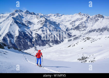 Frau back-country skiing aufsteigend in Richtung Punta Tre Chiosis, Blick auf Val Varaita mit Chianale, im Hintergrund der Monte Salza, Cima di Pienasea, Tete de Stockfoto