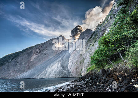 Grosse Ascheeruption mit auswürfen von Felsen am brennenden Rand von Batu Tara in der Flores See mit Leuchtdioden vulkanische Gase und Asche mit blauem Himmel. Ston Stockfoto