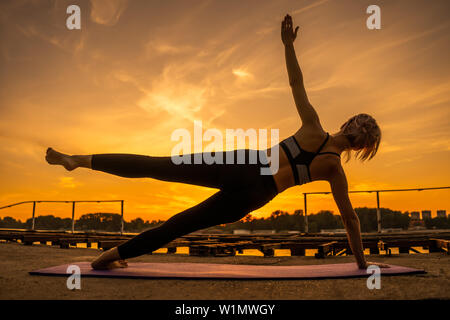 Frau Training Pilates in den Sonnenuntergang. Seitlicher Ganzkörperstütz mit Leg Kick Übung. Stockfoto