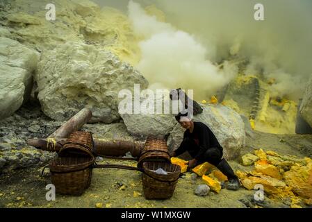 Minerworker zu giftiges Schwefeldioxid Gas der Mine ausgesetzt (Devil's mine) im Inneren des Vulkans Ijen auf der Insel Java und laden seine Körbe mit soliden Stockfoto