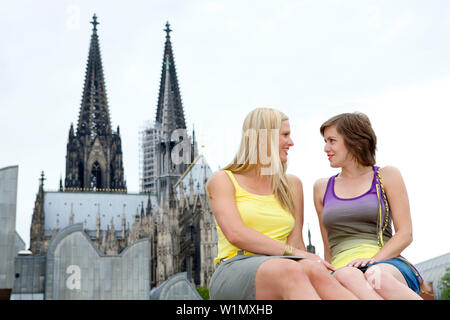 Zwei junge deutsche Frauen sitzen vor der Kathedrale von Köln, Köln, Nordrhein-Westfalen, Deutschland Stockfoto