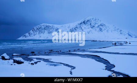 Verschneite Landschaft am Strand von Flakstad mit der Spitze des Hustinden (691 m) im Winter, Flakstadøya, Lofoten, Norwegen, Skandinavien Stockfoto