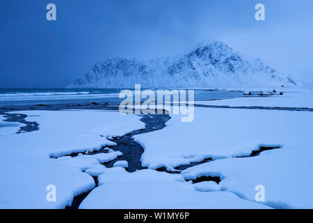 Verschneite Landschaft am Strand von Flakstad mit der Spitze des Hustinden (691 m) im Winter, Flakstadøya, Lofoten, Norwegen, Skandinavien Stockfoto