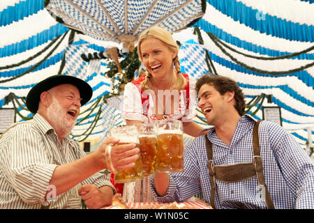 Paar und ein reifer Mann klirren Biergläser in einem Bierzelt Stockfoto