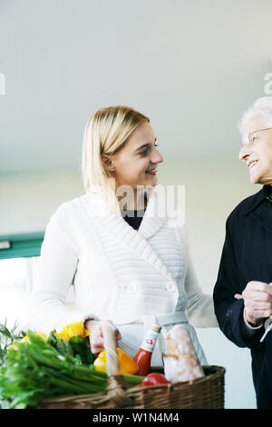 Junge Frau hilft, eine ältere Dame und trägt das Einkaufen Stockfoto