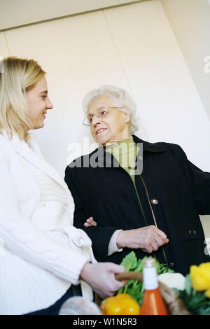 Junge Frau hilft, eine ältere Dame und trägt das Einkaufen Stockfoto