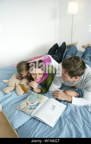 Junge Familie liegend auf Bett, während Sie ein Buch lesen, München, Deutschland Stockfoto