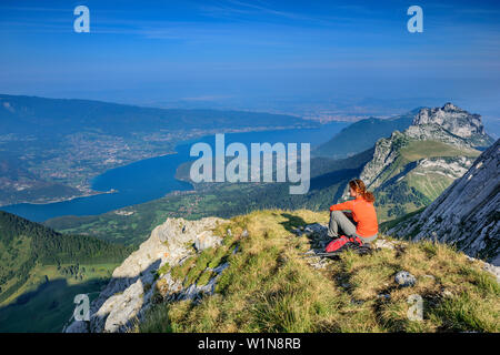 Frau wandern sitzen auf grasbewachsenen Felsvorsprung und Blick auf den Lac d'Annecy, Tournette, La Tournette, Haute-Savoie, Frankreich Stockfoto