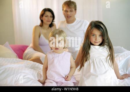 Junge Familie sitzt auf dem Bett, Porträt Stockfoto