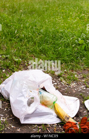 Zerknitterte Plastiktüte mit Müll und Wegwerf Utensilien auf dem Rasen im Park in der Nähe. Umweltverschmutzung. Müll, Dump, Kunststoffabfällen Verschmutzung Stockfoto