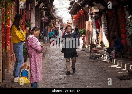 Tochter Farbstoffe ihre Mutter Haare auf der belebten Straße der alten Stadt Lijiang, Yunnan, China Stockfoto