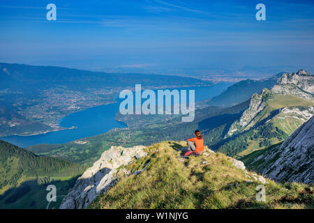 Frau wandern sitzen auf grasbewachsenen Felsvorsprung und Blick auf den Lac d'Annecy, Tournette, La Tournette, Haute-Savoie, Frankreich Stockfoto