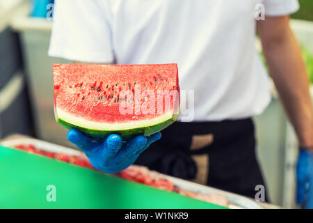 Koch in Gummi Handschuhe halten in der Hand und bietet großes Stück frischen leckeren saftigen Scheiben Wassermelone für Hotelgäste im Tropical Resort im Freien Stockfoto