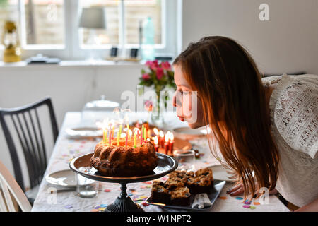 Junges Mädchen bläst die Kerzen auf der Geburtstagstorte bei Party in Hamburg, Deutschland Stockfoto