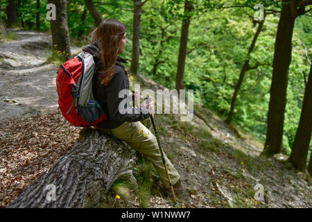 Junge Frau hat eine Pause auf einem Baumstamm beim Wandern durch den Wald auf dem Wanderweg Harzer Hexen stieg von Thale nach Treseburg, Frühling, Harz Forel Stockfoto