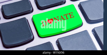 Nahaufnahme von einem grünen Knopf mit dem roten Buchstaben des Wortes Spenden, auf eine schwarze Tastatur. Stockfoto