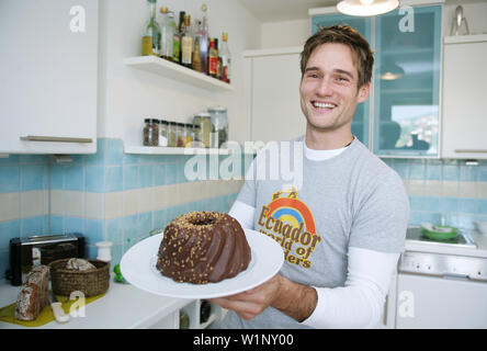 Lachende junger Mann hält einen Schokoladenkuchen, München, Deutschland Stockfoto