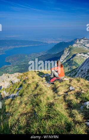 Frau wandern sitzen auf grasbewachsenen Felsvorsprung und Blick auf den Lac d'Annecy, Tournette, La Tournette, Haute-Savoie, Frankreich Stockfoto