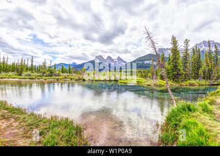 Die Canmore berühmten Three Sisters Berggipfel an der Polizist Creek in den Kanadischen Rocky Mountains von Alberta, Kanada. Die Berge reflektiert die Oberfläche Stockfoto