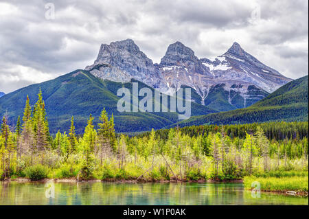 Die Canmore berühmten Three Sisters Berggipfel neben dem Bow River im südlichen Banff Spektrum der Kanadischen Rockies an einem bewölkten Frühling Morgen. Die Stockfoto