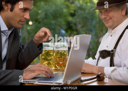 Alte bayerische Mann und junge Unternehmer mit Laptop im Biergarten, Starnberger See, Bayern, Deutschland Stockfoto