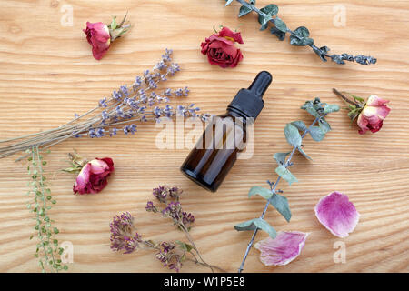 Ätherisches Öl mit Kräutern und Blumen auf Holz- Hintergrund Stockfoto