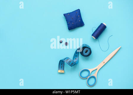 Nähzubehör mit Gewinde, Schere, Stifte, Stoff, Knöpfe und nähen Tape auf blauem Hintergrund. Ansicht von oben. Flach. Stockfoto