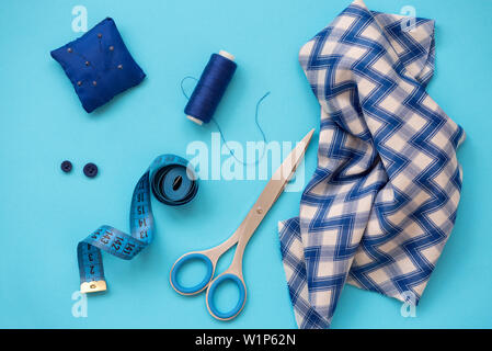 Nähzubehör mit Gewinde, Schere, Stifte, Stoff, Knöpfe und nähen Tape auf blauem Hintergrund. Ansicht von oben. Flach. Stockfoto