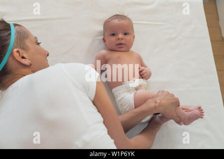 Ein Porträt von einem schönen Kind und eine Frau es halten an einer Tabelle ändern. Baby Massage. Stockfoto