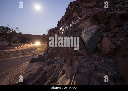 Ein Geländewagen durch die Doros trockenes Flussbett unter dem Vollmond im Damaraland, Kunene, Namibia fahren Stockfoto