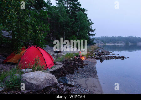 Kleinen Jungen neben dem roten Zelt sitzt am Lagerfeuer im Archipel Insel Fiskhamn, Stockholm, Schweden Stockfoto