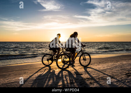 Zwei Radfahrer auf dem Strand am Golf von Mexiko bei Sonnenuntergang, Fort Myers Beach, Florida, USA Stockfoto