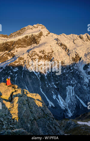 Frau sitzt auf Felsen und Blick auf Mount Sefton und Hocker, von Mueller Hut, Hooker Valley, Mount Cook Nationalpark, UNESCO Welterbe Te Wa Stockfoto