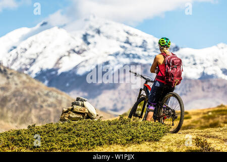Junge Frau nimmt eine Pause auf Ihrem Mountainbike und genießt die Aussicht auf die Ortlergruppe, Bormio, Sondrino, Lombardei, Südtirol, Italien Stockfoto