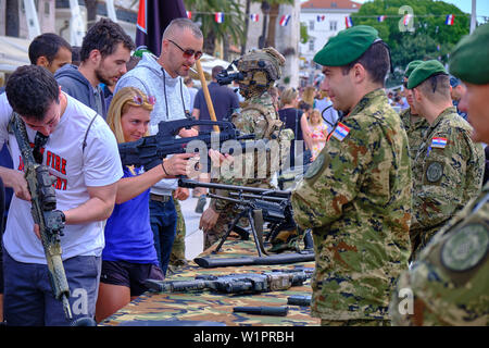 Split, Kroatien - 27. April 2019. Kroatische militärische Ausstellung. Junge blonde Frau herauf Waffe auf Anzeige und darauf abzielen, amüsiert Soldat Stockfoto