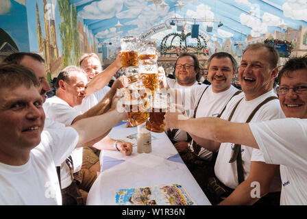 Männer im mittleren Alter heben ihr Bier mugsto Toast auf dem Oktoberfest, München, Bayern, Deutschland Stockfoto