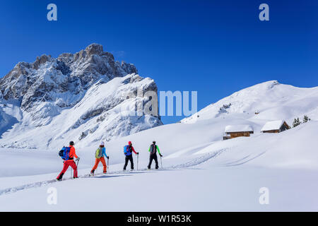 Mehrere Personen backcountry Skiing aufsteigender Richtung Almhütten, Geisler Bereich im Hintergrund, Medalges, Naturpark Puez-Geisler, UNESCO-herit Stockfoto