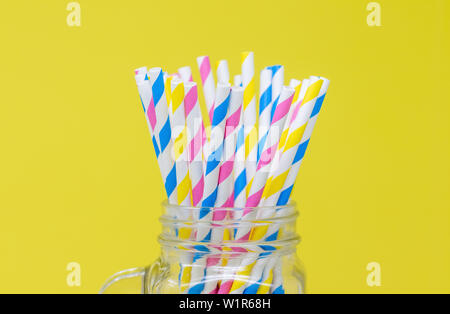Bunte Papier Trinkhalme im Glas. mit einem gelben Hintergrund. Nahaufnahme mit einer geringen Tiefenschärfe. Stockfoto
