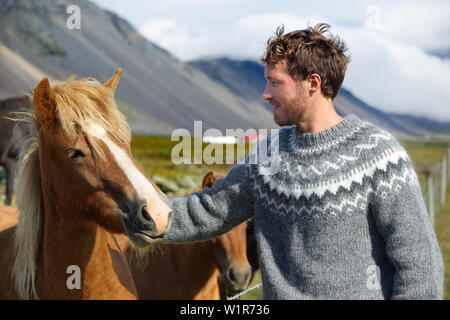 Islandpferde - Mann petting Pferd auf Island. Mann in Isländische Pullover gehen Reiten lächelt glücklich mit Pferd, in schöner Natur auf Island. Schöne skandinavische Modell. Stockfoto