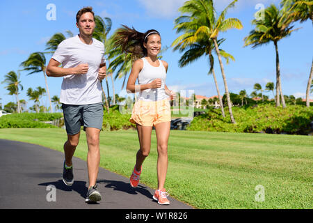 Sport paar Ausübung außerhalb auf Straße im Sommer. Gerne aktive junge Erwachsene fit Jogging zusammen mit tropischen Hintergrund im Stadtpark oder Resort Road. Asiatische und kaukasischen Völker. Stockfoto