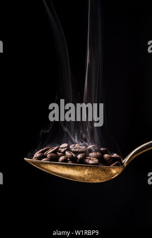 Close-up einen Löffel mit gerösteten Kaffeebohnen heiß vor dem dunklen Hintergrund aromatisiert Stockfoto